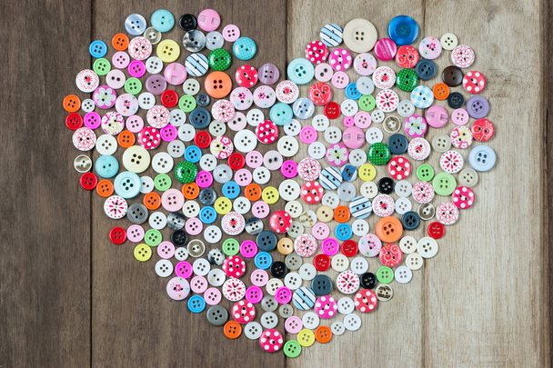 Colección de botones usados en forma de corazón sobre fondo de madera
. - Foto, Imagen
