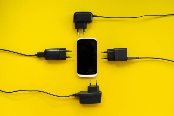 Smartphone and chargers around on a yellow background, concept. - Foto, afbeelding