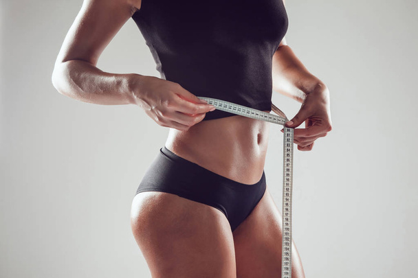 Atletica donna magra misurare la sua vita da nastro di misura su sfondo bianco
 - Foto, immagini