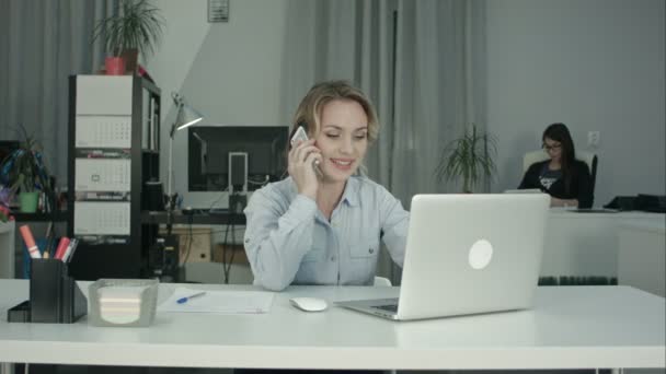 Two female coworkers working together answering phone calls in the office - Filmati, video