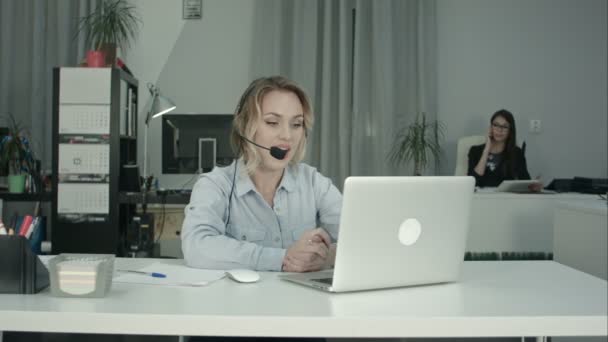 Smiling call center operator working with laptop using headset in office - Footage, Video