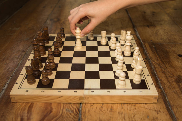 a single hand playing chess on a wooden board set on some wooden - Fotografie, Obrázek
