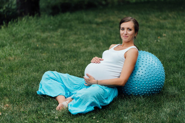 妊娠中のヨガ出生前フィット ボールのさまざまな演習を行います。呼吸、ストレッチ、ピラティス、草の上の公園で. - 写真・画像