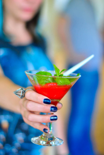 Punainen mansikka cocktail kädessä tyttö on epätarkka. Hedelmäcocktail lasissa. Tausta hämärtyy. Mansikkapirtelöt
. - Valokuva, kuva