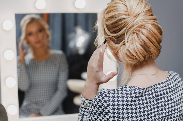 Mooie vrouw met kapsel en make-up te kijken naar de spiegel in de beauty salon een - Foto, afbeelding