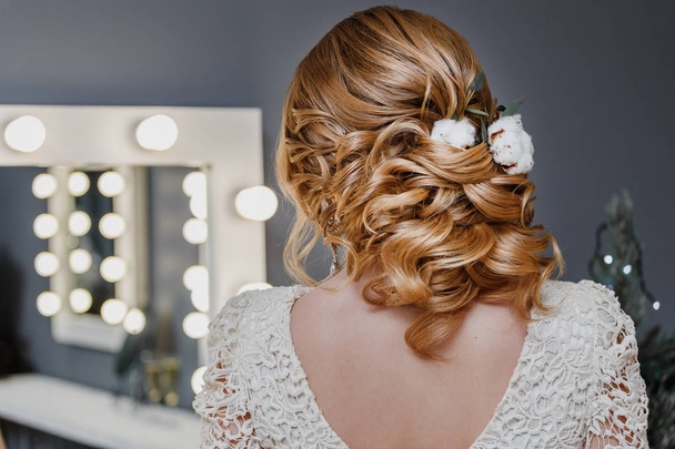 Fiatal gyönyörű homokos hajú nő, stílusos frizurát pamut virág egy bézs ruha preens közel a tükör, lámpával, szépségszalon - Fotó, kép