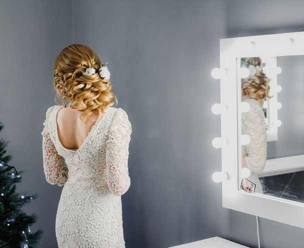 ベージュのドレスに綿の花でスタイリッシュな髪型の若い美しい砂髪の女性は美容院でランプとミラーの近く得意します。 - 写真・画像