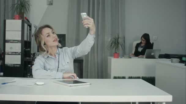 Gyönyörű fiatal irodai dolgozó vesz selfies telefont használ fejhallgató - Felvétel, videó