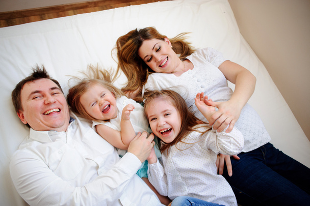 Big close-knit family from four people cheerfully spends time for beds - Photo, Image