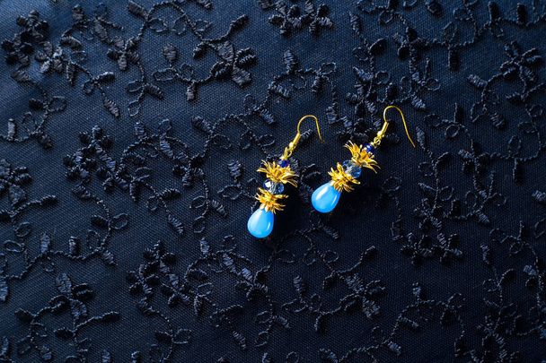 Macro photo of jewelry on the textured background. Small Golden earrings with blue glass beads - Photo, Image