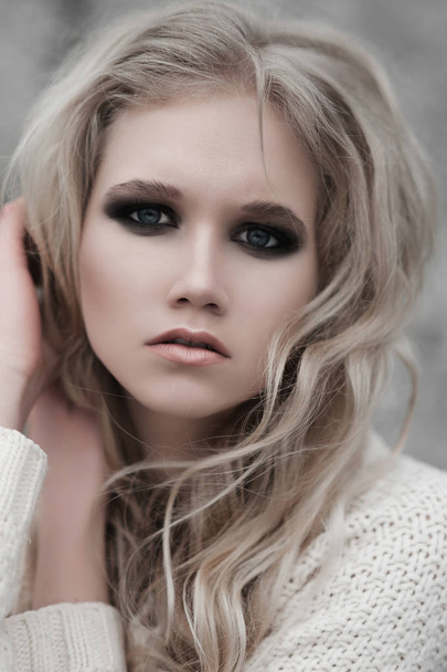 Крупним планом красива молода блондинка з блакитними очима в білому пуловері
. - Фото, зображення