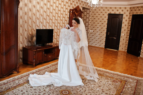 Cute brunette bride on silk robe with wedding dress on hands. - Foto, Bild
