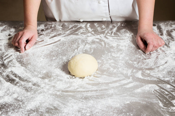 Femme pétrir la pâte dans la boulangerie, sur une table en acier. Processus de travail
. - Photo, image