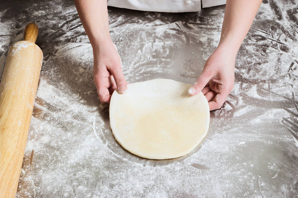 Woman unrolls dough in bakery, on a table from steel. Working process. - Foto, afbeelding