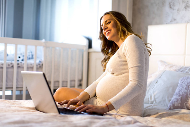 ベッドでノート パソコンを妊娠中の女性 - 写真・画像