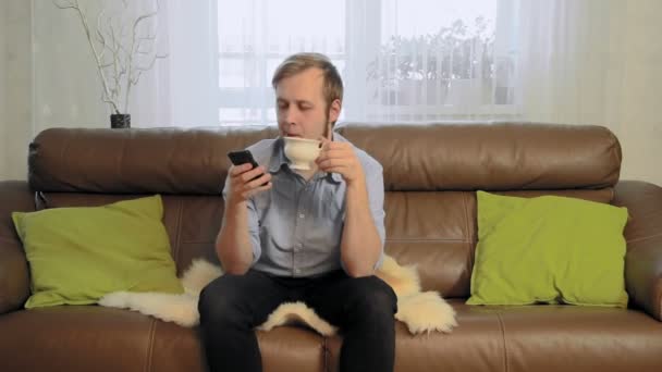 Young man drinking tea and using his phone - Felvétel, videó