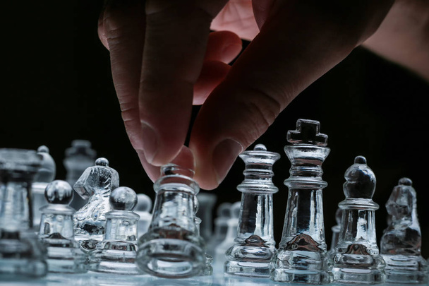 Vista de perto no tabuleiro de xadrez de vidro transparente com mão masculina
 - Foto, Imagem