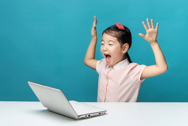 sorprendida, linda niña asiática que disfruta de la computadora portátil sobre fondo azul
 - Foto, Imagen