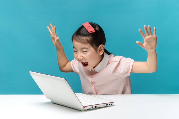sorprendida, linda niña asiática que disfruta de la computadora portátil sobre fondo azul
 - Foto, Imagen