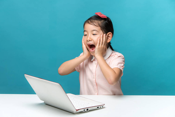 meglepett, aranyos ázsiai kislány, akik élvezik a hordozható számítógépet a kék háttér - Fotó, kép