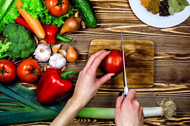 Verduras y verduras frescas rojas y verdes acostadas sobre una superficie de madera. En una tabla de madera chef rebanando tomate
. - Foto, Imagen