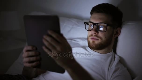 man with eyeglasses and tablet pc in bed at night - Imágenes, Vídeo