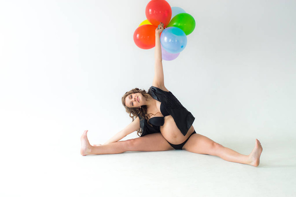 Pregnant woman with balloons and hands above head sit on floor - Photo, image