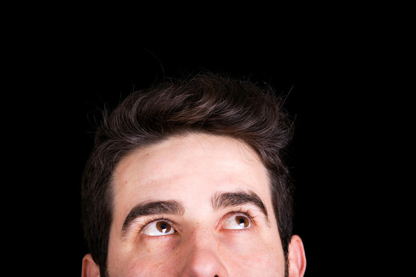 Young handsome man looking up, against black background - Photo, Image