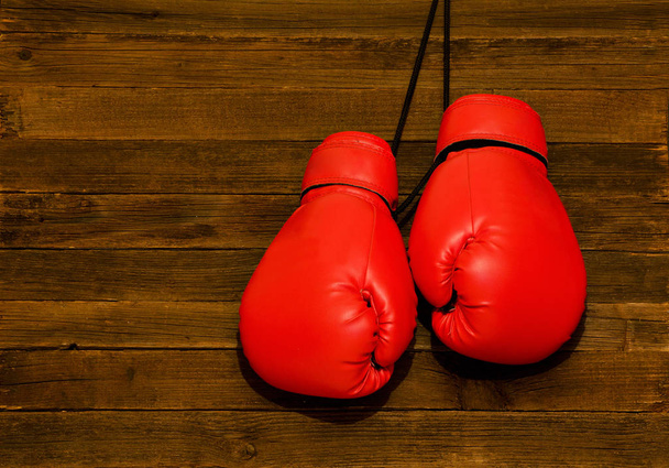 Dvě červené Boxerské rukavice zavěšené na dřevěné hnědé pozadí, prázdné místo - Fotografie, Obrázek
