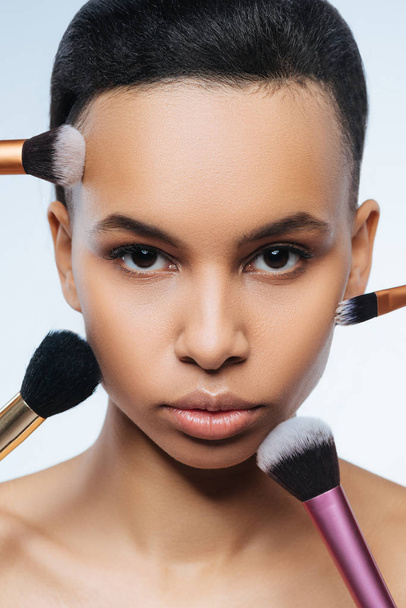 Close up of womans face surrounded by cosmetic brushes - Photo, image