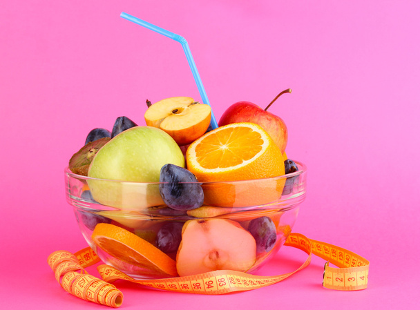Glass bowl with fruit for diet and measuring tape on pink background - Photo, Image