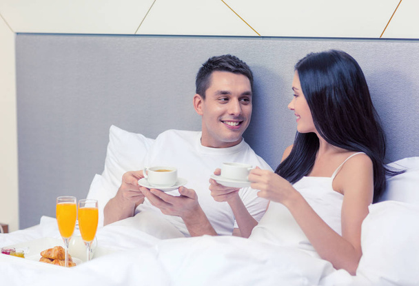 smiling couple having breakfast in bed in hotel - Fotoğraf, Görsel