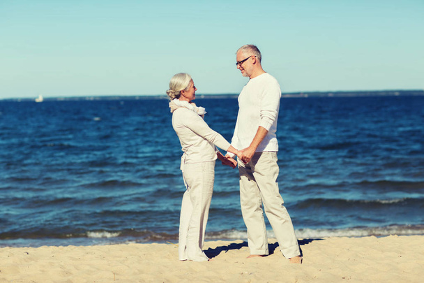 happy senior couple holding hands on summer beach - Фото, изображение
