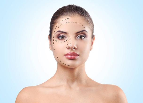 Young woman with marks on face against blue background. Plastic surgery concept - Фото, изображение
