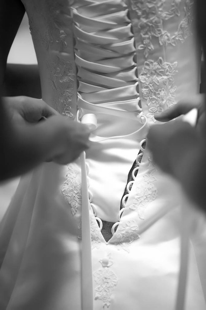 hands tying a wedding dress, close-up of brides back in white wedding dress, black and white photo - Photo, Image
