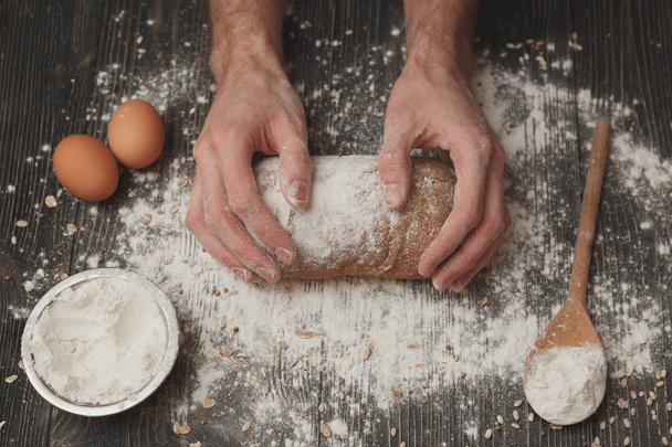 Close-up of men's baker hands on black bread with flour powder. Baking and patisserie concept - Fotografie, Obrázek