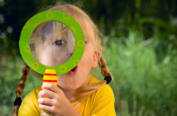 Girl with surprise looks through a magnifying glass - Photo, Image