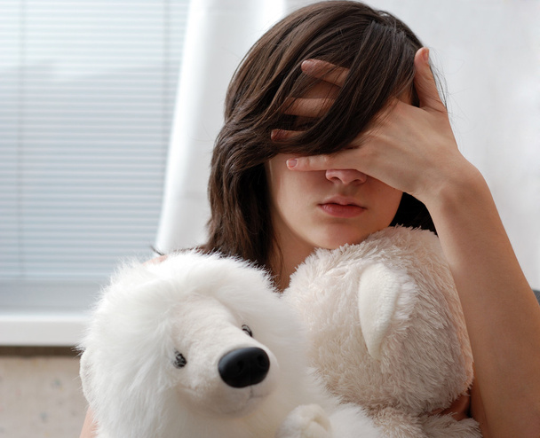 Девочка-подросток с плюшевым мишкой, лицо скрыто рукой
 - Фото, изображение