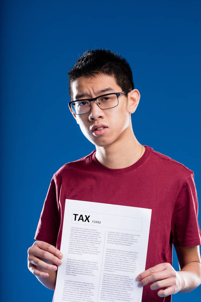 сумнівний азіатський чоловік тримає податкову форму
 - Фото, зображення