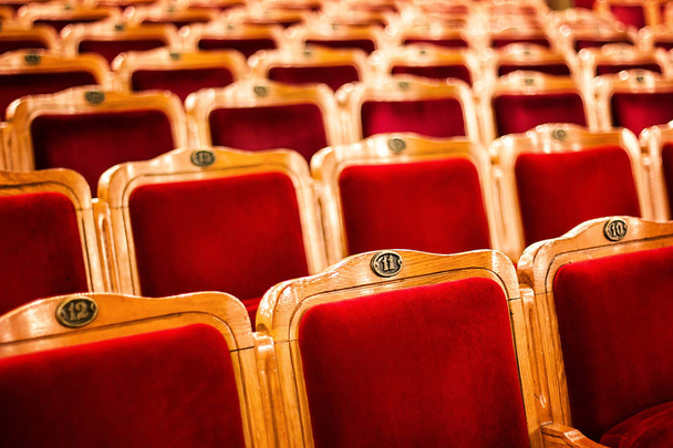 Sets on an empty theatre, taken with selective focus and shallow depth of field. Empty vintage red seats with numbers, teather chair, cinema seats. Movie theater auditorium with lines of red chairs. - Photo, Image