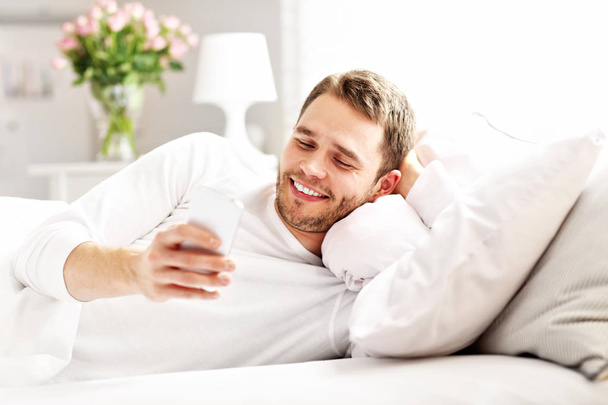 Mann liegt mit Smartphone im Bett - Foto, Bild