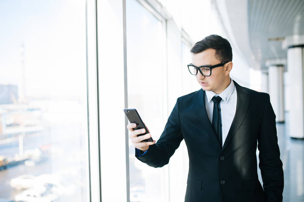Pohledný podnikatel v obleku mobilní telefon umožňuje zkontrolovat e-mail nebo napsat zprávu v místnosti úřadu - Fotografie, Obrázek