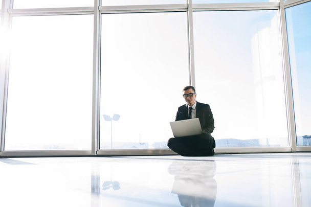 homem de negócios no chão com laptop em janelas panorâmicas
 - Foto, Imagem