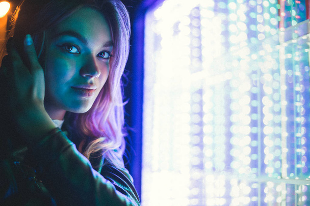 Menina posando em um fundo de dispositivos de luz brilhante. Close-up de um modelo de rosto iluminado em cores diferentes
. - Foto, Imagem