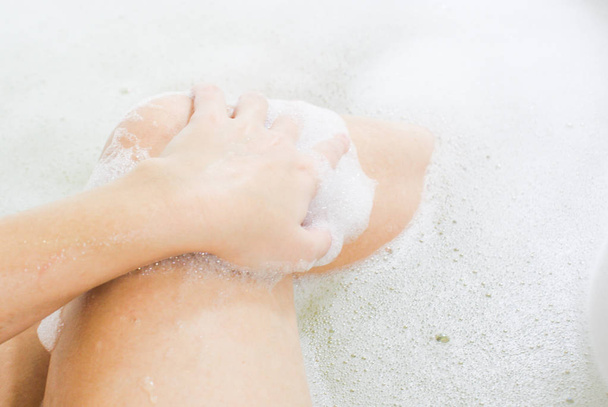  De slanke benen van de vrouw in een bad met geurige schuim - Foto, afbeelding