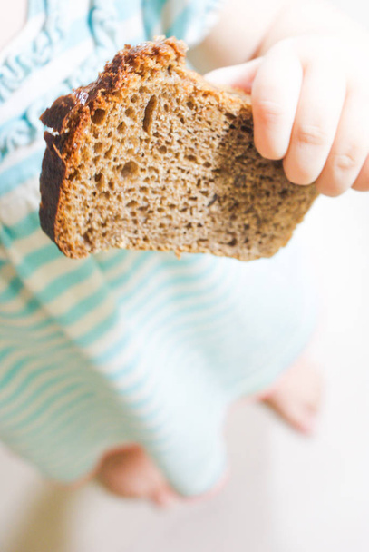 Kinderhand nimmt ein Stück frisches Brot mit Gewürzen, Rosinen und Nüssen - Foto, Bild