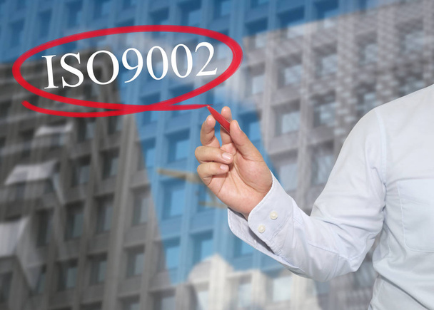A mão do jovem homem de negócios escreve a palavra ISO 9002 em arranha-céus
 - Foto, Imagem