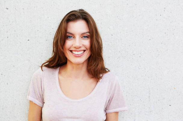 Nuori nainen hymyilee seinää vasten
 - Valokuva, kuva