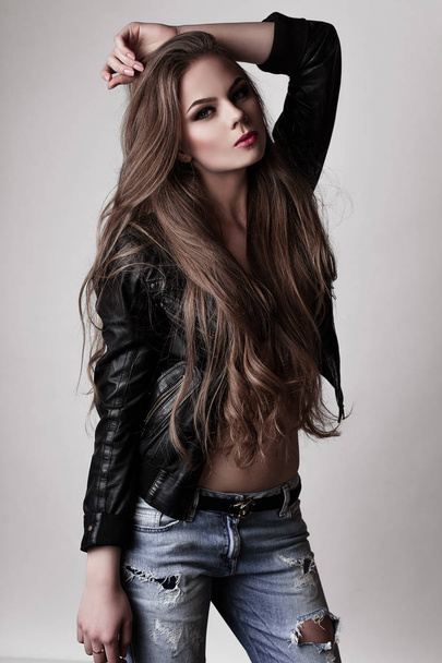 Young girl with long beautiful hair and smoky eyes wearing black leather jacket and jeans . Studio shot.  - Photo, Image