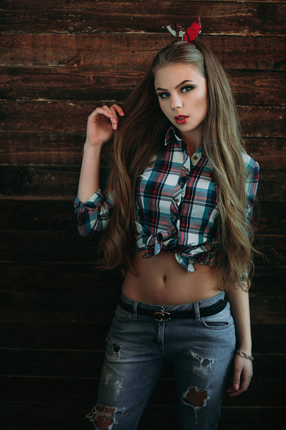 Menina jovem atraente sorrindo com aparência de país, tiro de estúdio, estilo country americano. Fundo de madeira
  - Foto, Imagem
